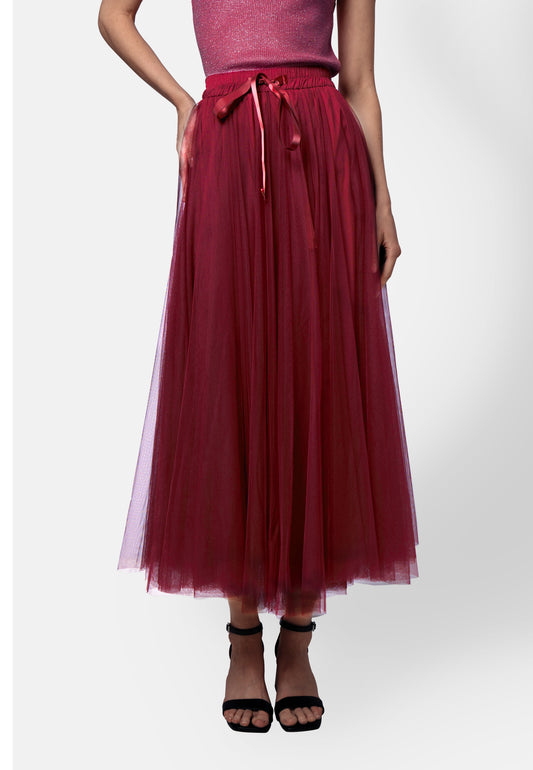 Model trägt einen beerenroten Midirock aus mehrlagigem Tüll mit Satinband in der Taille, kombiniert mit einem pinken Glitzer-Top und schwarzen Sandaletten.