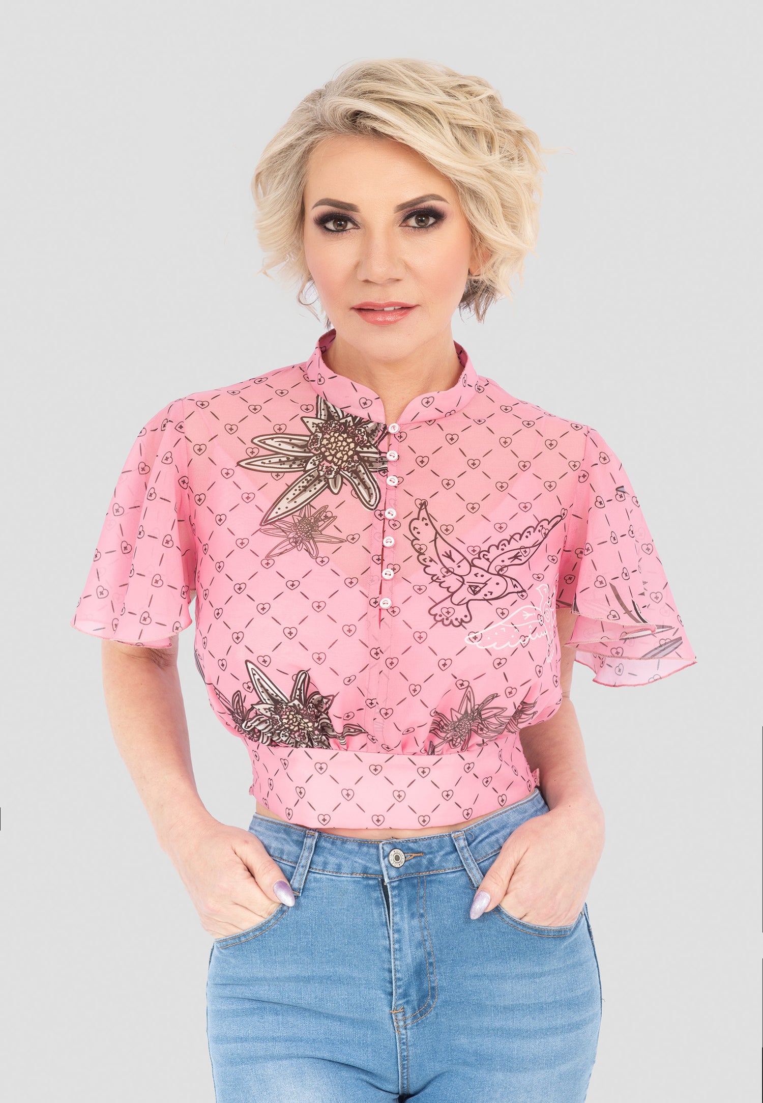 Die Design Edelweiß Top-Bluse mit Knöpfen in Rosa ist ein lässiges und zugleich stilvolles Oberteil. Sie ist mit einem elastischen, gesmokten Bündchen am Rücken ausgestattet, was für eine bequeme Passform sorgt. Die Bluse hat eine normale Passform, kurze Ärmel und ist kurz geschnitten. Gefertigt aus einer leichten Mischung aus 40 % Viskose und 60 % Polyester, bietet sie hohen Tragekomfort und ist ideal für den Alltag. Unser Model ist 171 cm groß und trägt Größe M.