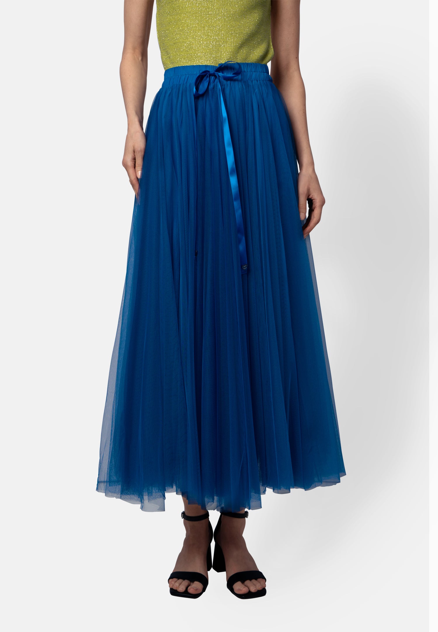 Model trägt einen weit schwingenden Midirock aus kobaltblauem Tüll mit glänzendem Satinband in der Taille, kombiniert mit einem limonengelben Oberteil und schwarzen Sandaletten.